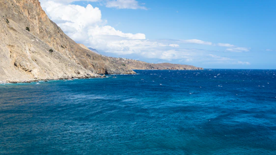 A sweeping aerial view of a rugged coastline meeting the deep blue ocean under a clear sky.
