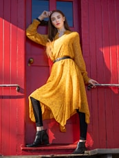 woman in yellow long sleeve shirt and black pants leaning on red wooden door