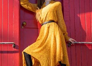 woman in yellow long sleeve shirt and black pants leaning on red wooden door