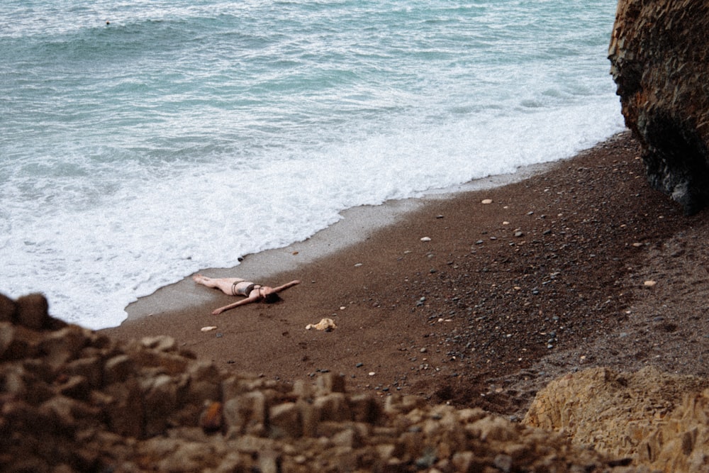 person in white shirt sitting on brown sand near sea during daytime