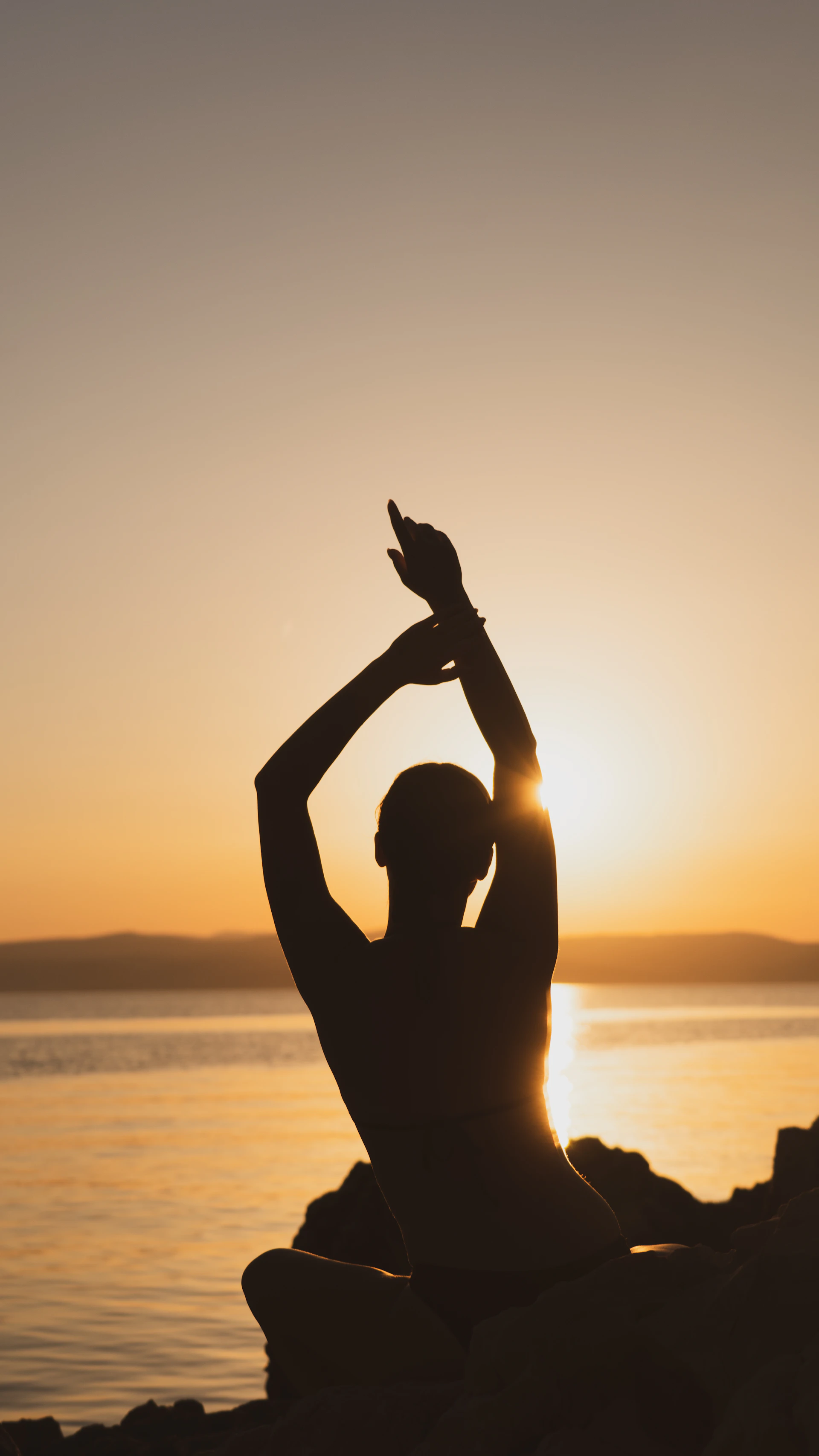 Silhouette of a person raising their hands at sunset