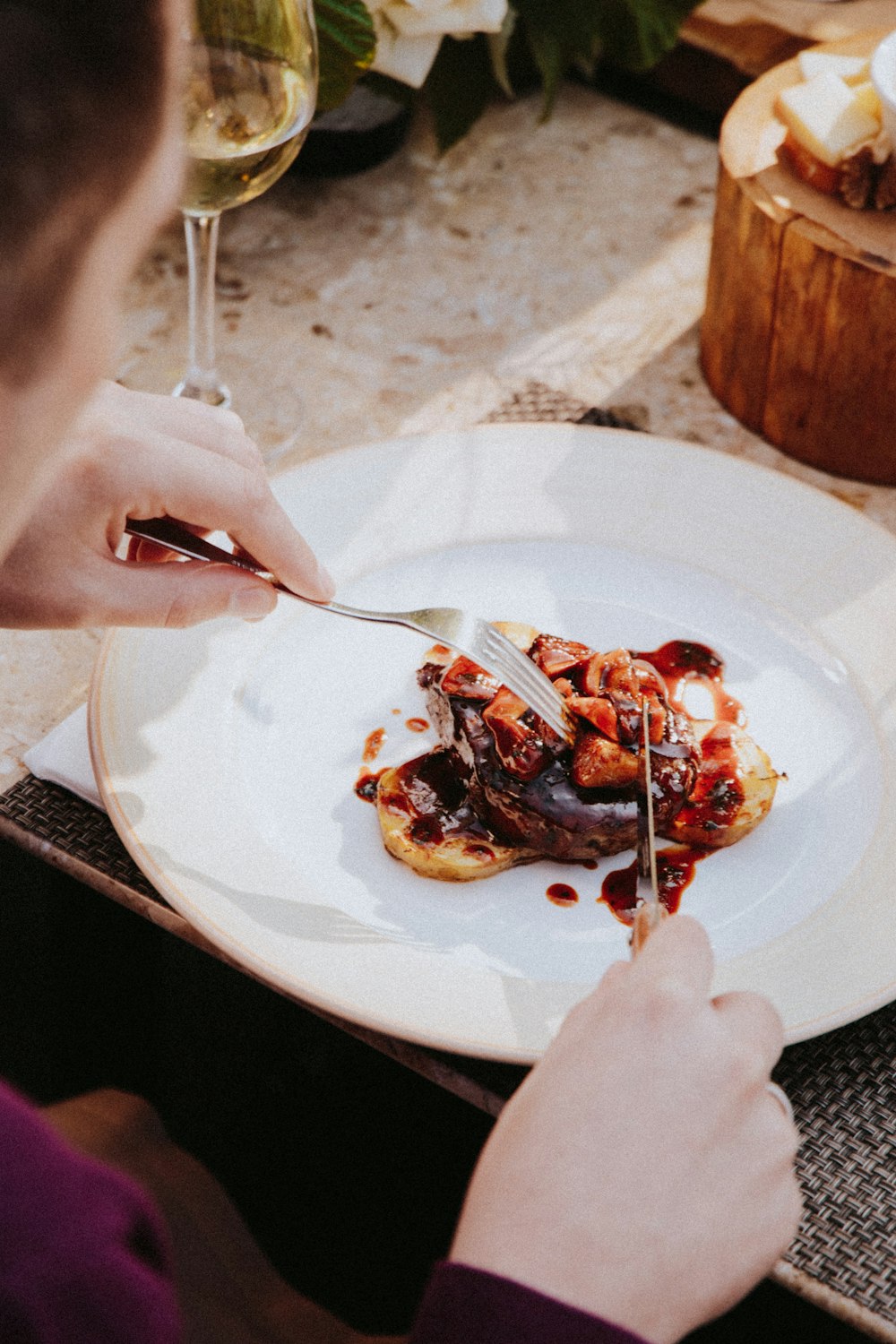 person holding stainless steel fork and knife slicing strawberry cake on white ceramic plate