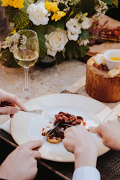 person holding stainless steel fork and knife slicing cooked food on white ceramic plate