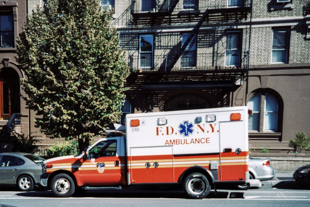 Furgoneta ambulancia blanca y roja estacionada cerca de árboles verdes durante el día