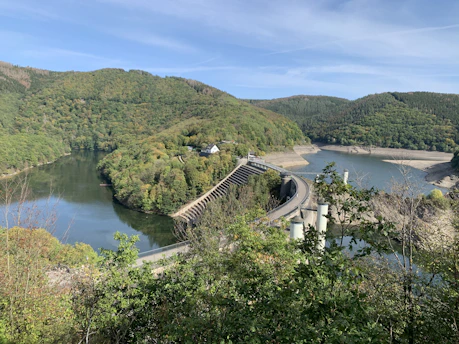 A panoramic view of a large earth dam under construction amidst rolling hills.