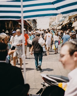 A bustling city street filled with people shopping at colorful outdoor markets under bright sunlight.