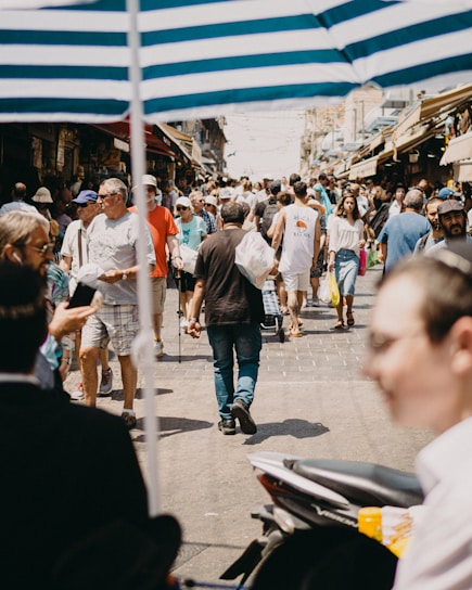 A bustling city street filled with people shopping at colorful outdoor markets under bright sunlight.