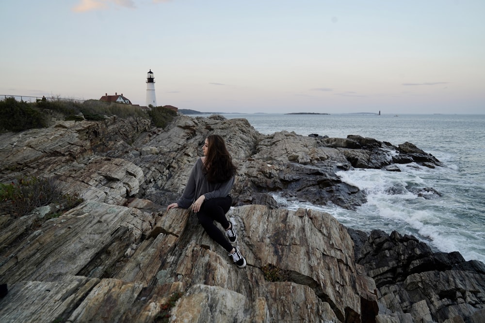 woman in black jacket sitting on rock formation near sea during daytime