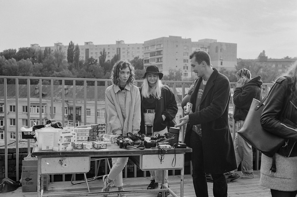 grayscale photo of 3 men standing beside table