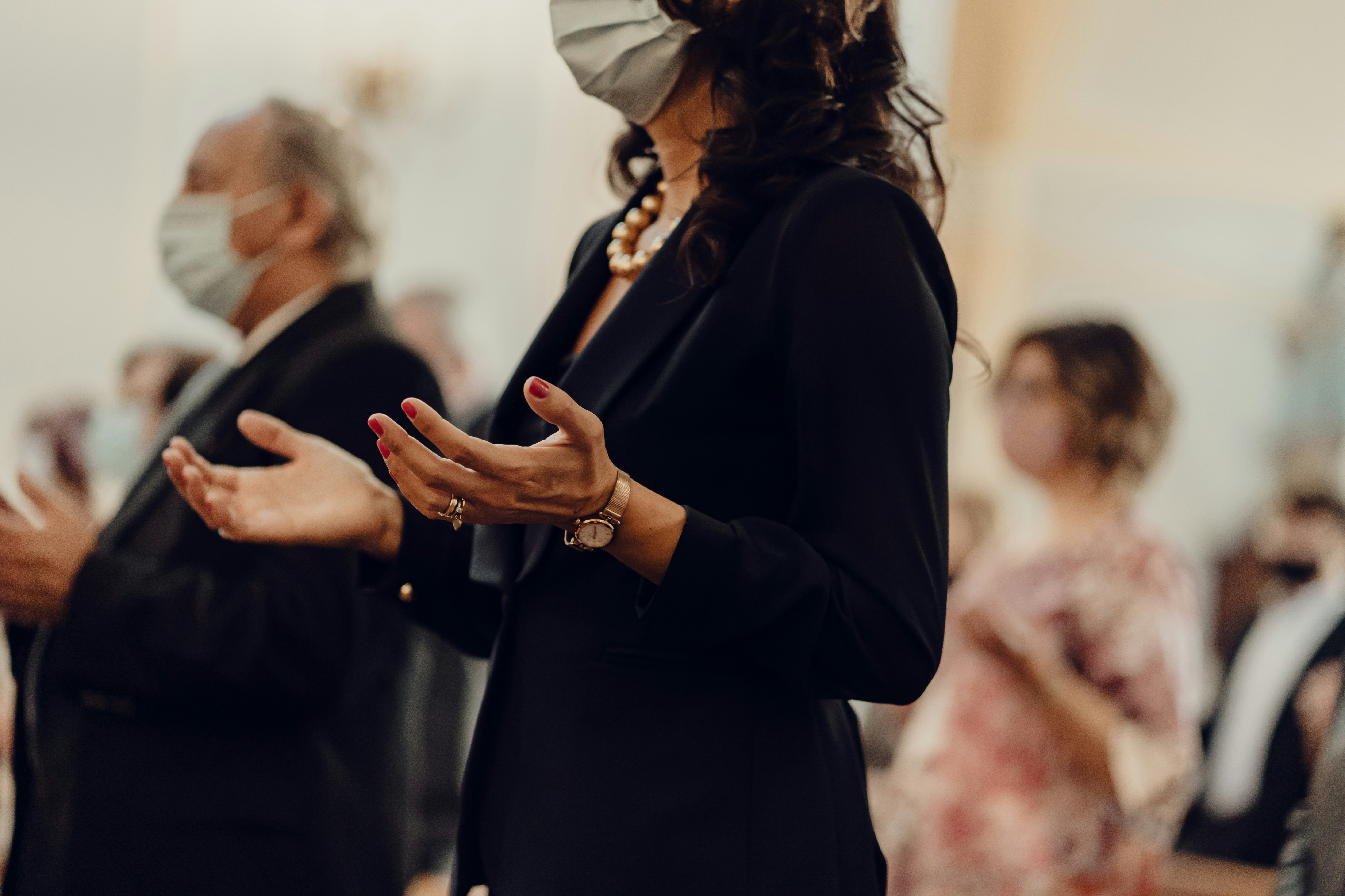 Woman in church wearing a face mask and praying with her hands outstretched