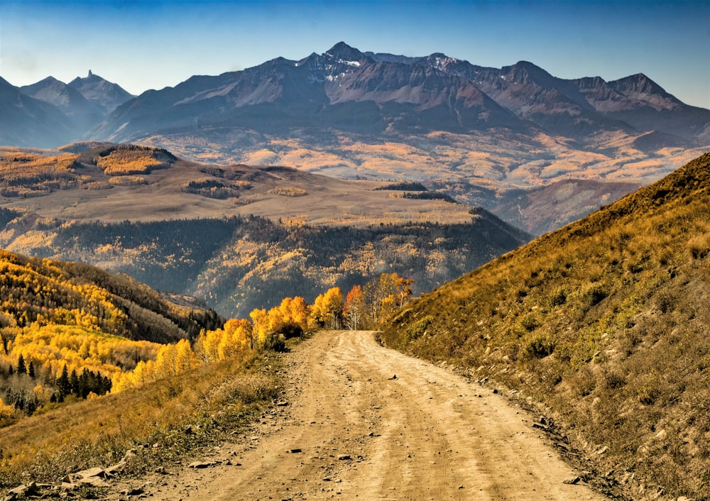 brown dirt road between green grass field and mountains during daytime