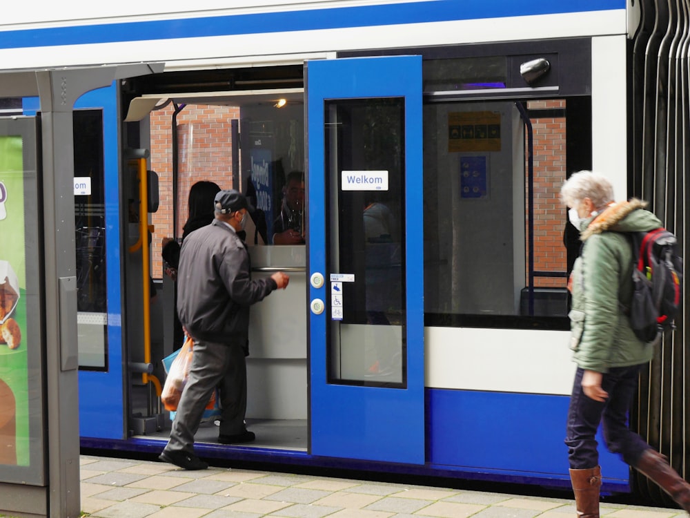 man in gray jacket standing beside blue and white train during daytime