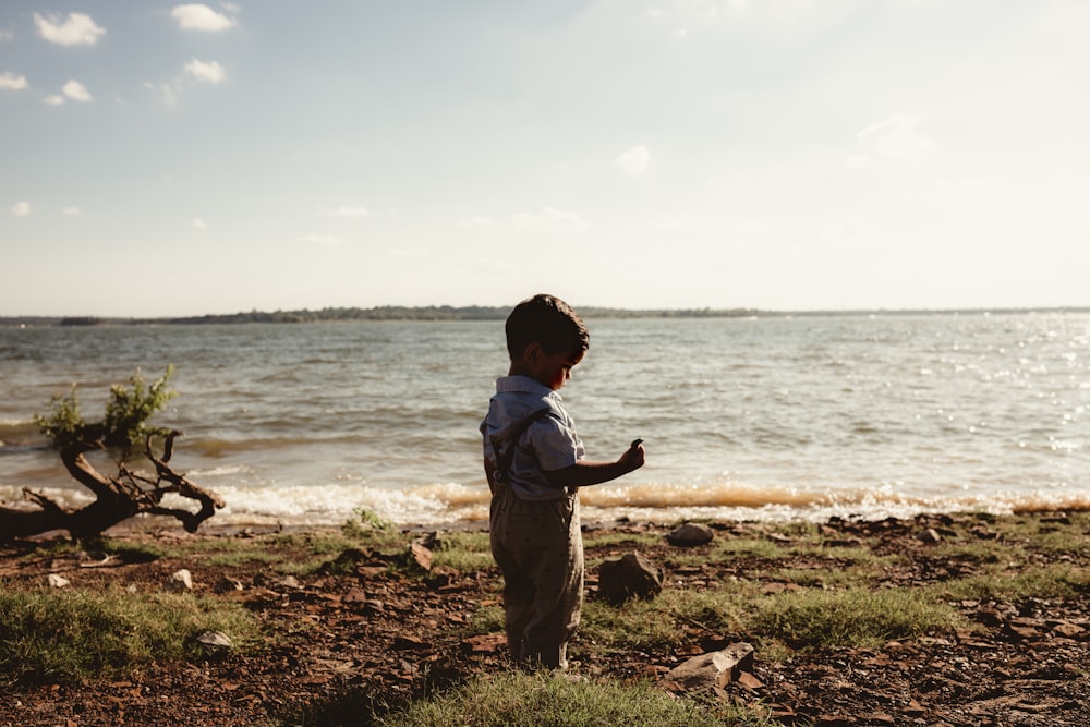 boy in gray shirt standing on brown field near body of water during daytime
