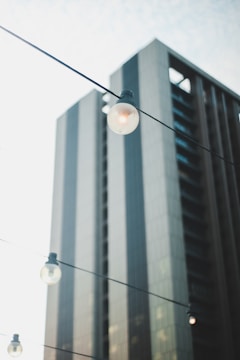A modern skyscraper with sleek, reflective surfaces stands tall in the background. In the foreground, several lightbulbs are suspended on wires, adding a touch of urban aesthetics. The overall scene is calm, with a soft, diffused light creating a serene atmosphere.