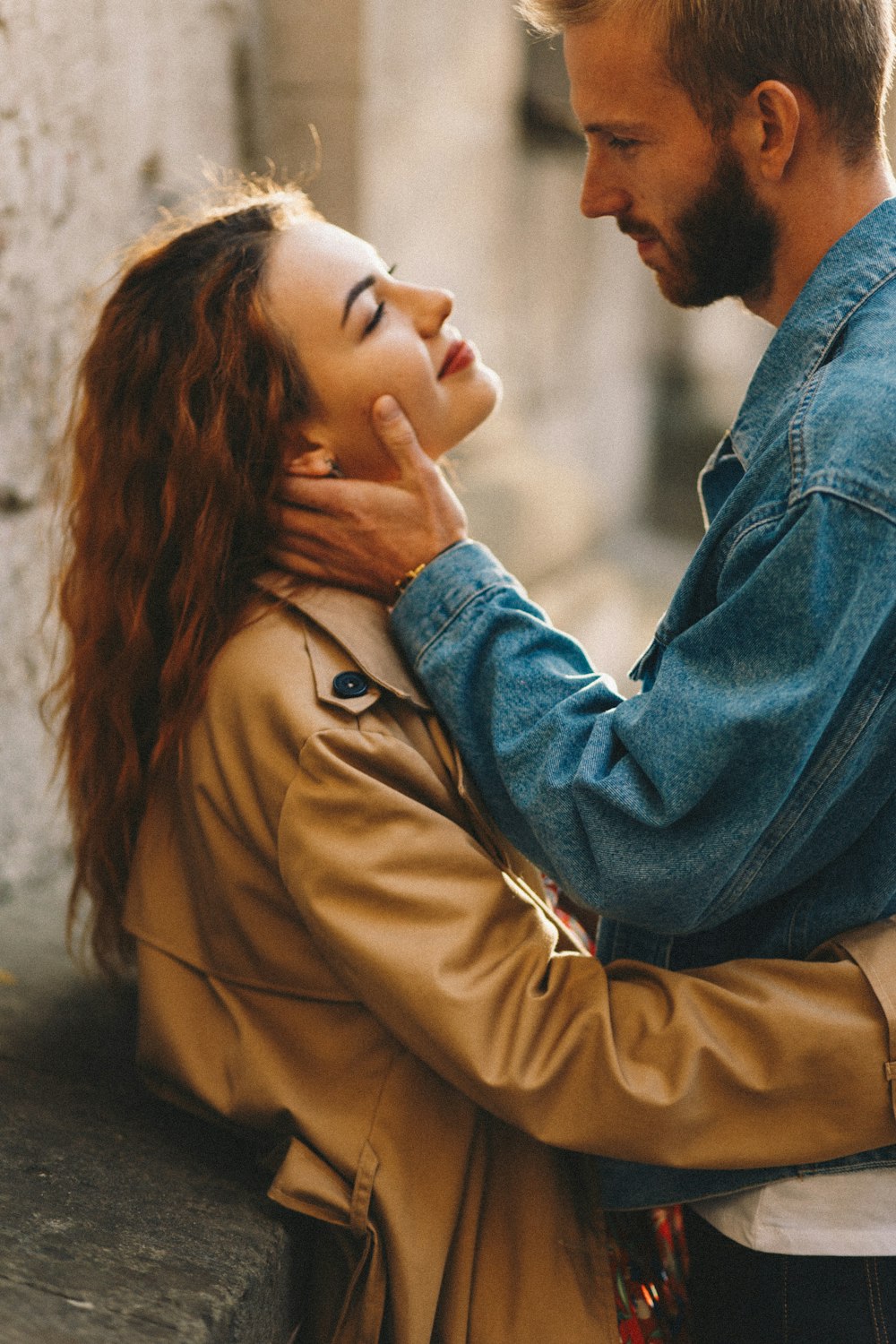 man in blue denim jacket kissing woman in brown coat