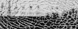A close-up of shattered glass with jagged, irregular shapes interlocking across the frame. The fragmented glass pieces create a chaotic pattern with a blurred background.