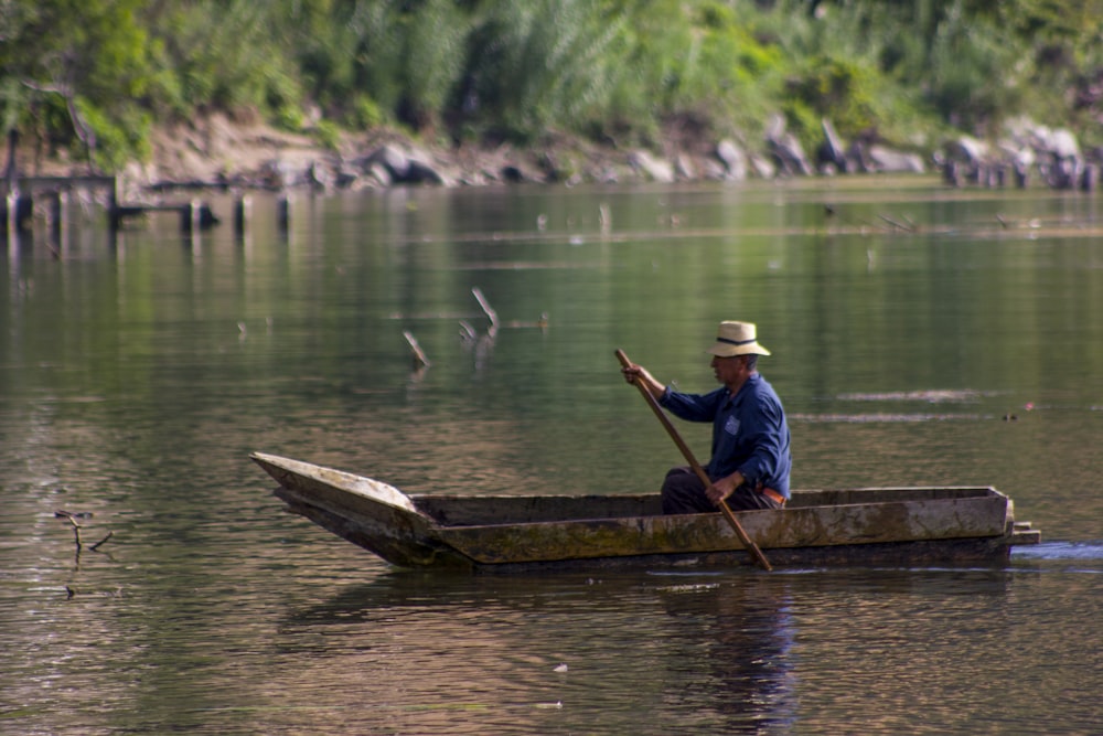 homem na camisa azul e boné branco sentado no barco de madeira marrom durante o dia