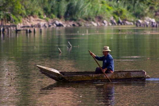man in blue shirt and white cap sitting on brown wooden boat during daytime in San Juan La Laguna Guatemala