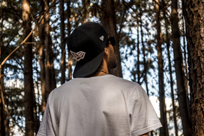 man in gray shirt wearing black cap standing in forest during daytime