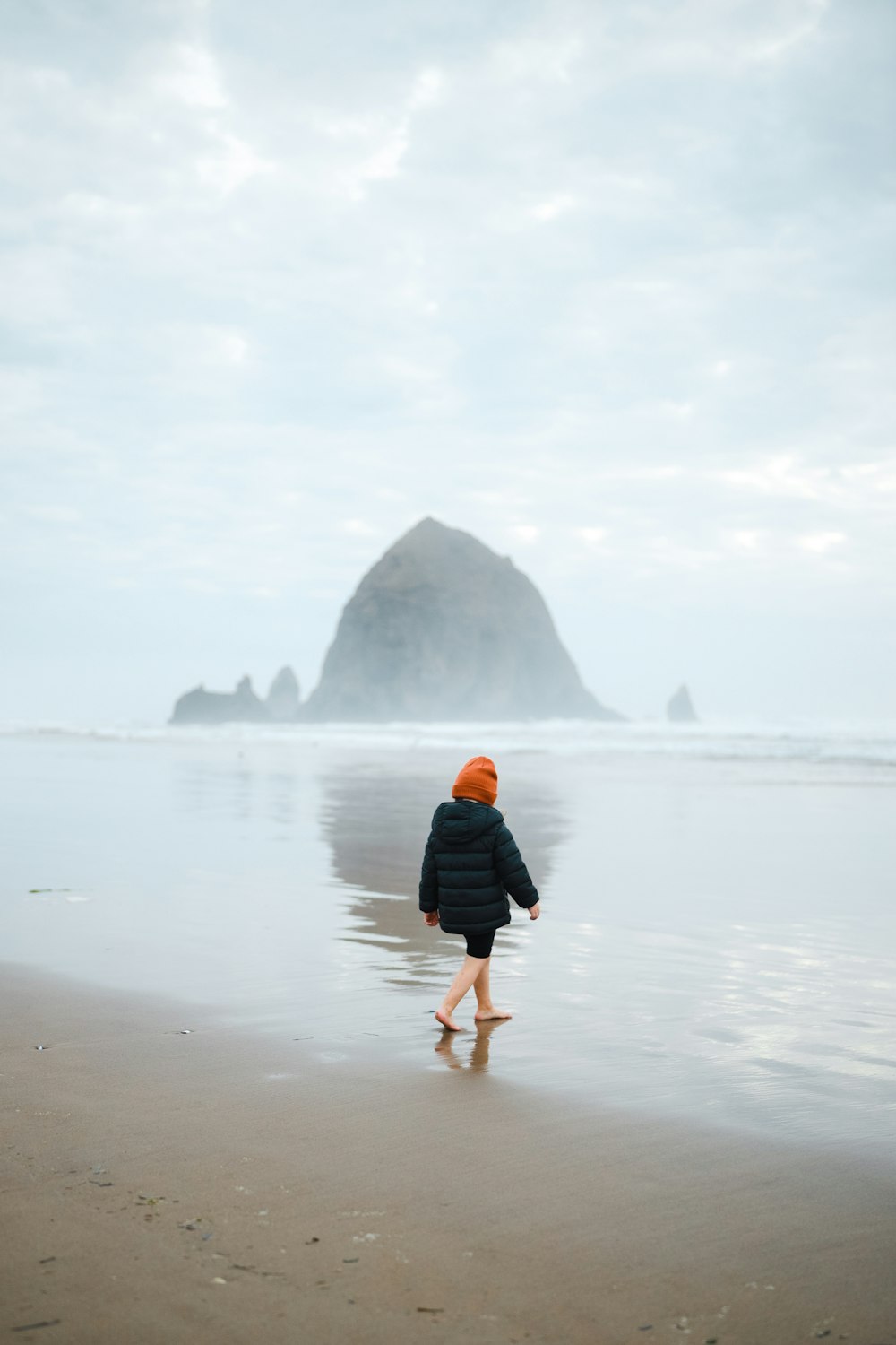 woman in black jacket walking on seashore during daytime