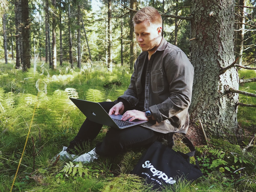 man in black jacket sitting on green grass field using laptop computer
