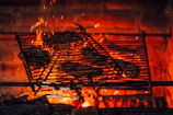 Grilled meat sizzling over an open flame with smoke rising.