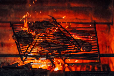 Grilled meat sizzling over an open flame with smoke rising.