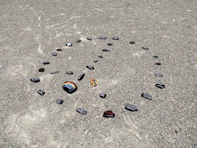 Hand-painted memorial stones laid gently on a mossy riverbank, each stone bearing a name and message.
