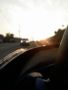 A young woman happily driving a compact car on an open road during sunset.