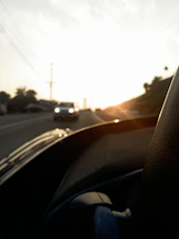 A friendly driving instructor chatting with a student beside a car, warm sunset lighting