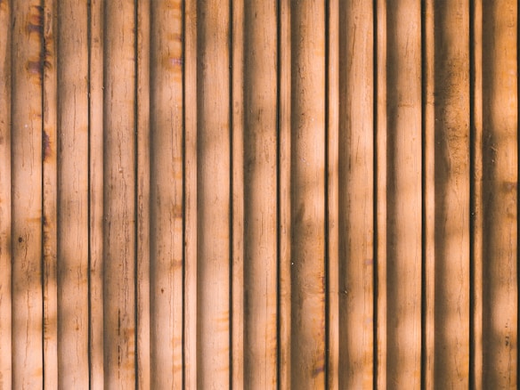 Vertical wooden planks with a natural brown color, featuring subtle shadows and variations in texture and grain.