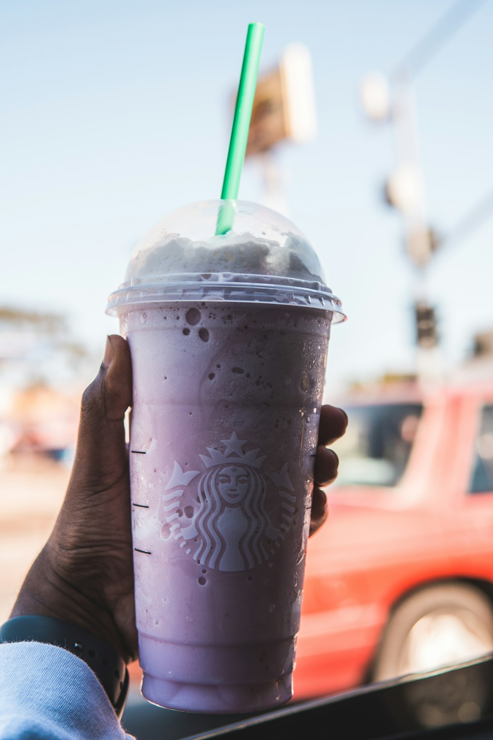 person holding starbucks disposable cup with green straw