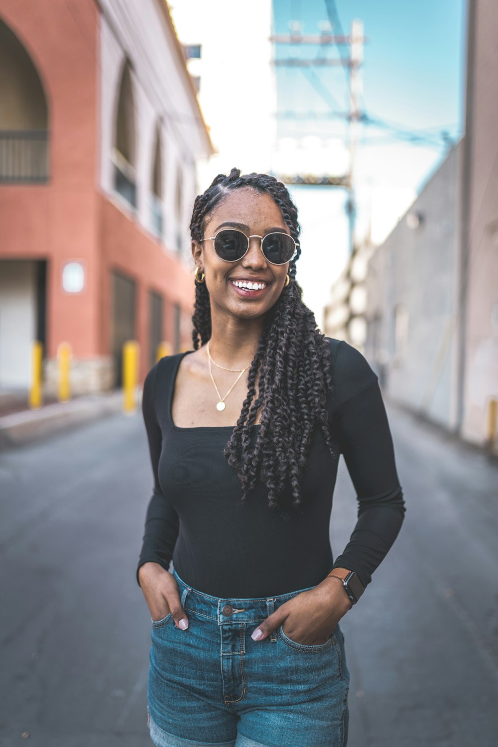 woman in black long sleeve shirt and blue denim jeans wearing sunglasses standing on road during