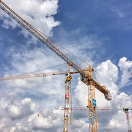 A construction site with cranes lifting steel beams against a clear blue sky.