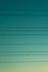 High tension power lines are visible against a serene gradient sky transitioning from dark turquoise to pale cyan.