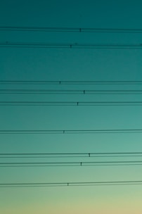 High tension power lines are visible against a serene gradient sky transitioning from dark turquoise to pale cyan.