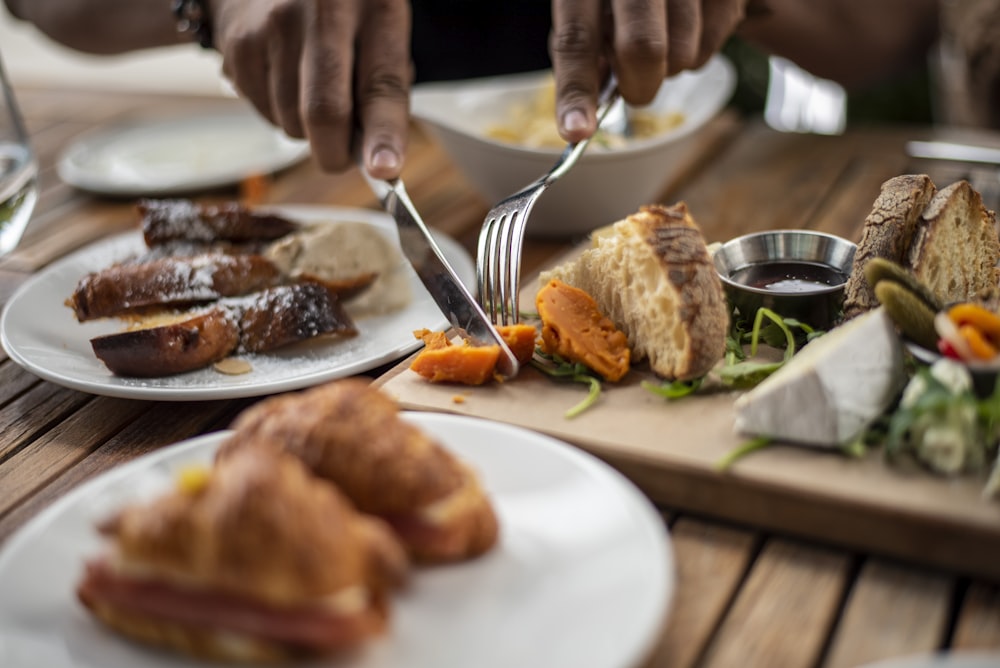 person holding stainless steel fork and knife slicing cooked food on white ceramic plate