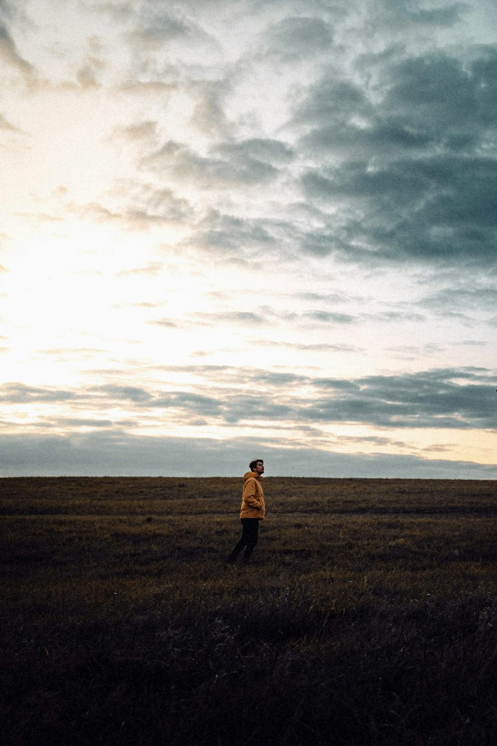 man in brown jacket standing on brown field under white clouds during daytime