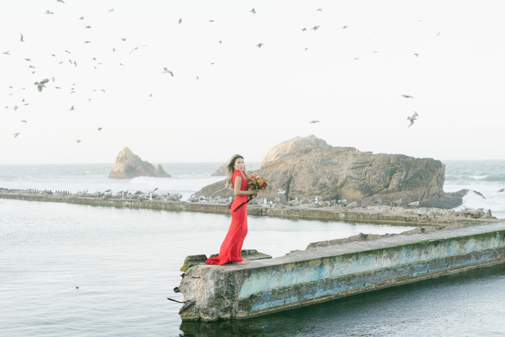 woman in red dress standing on gray concrete dock during daytime