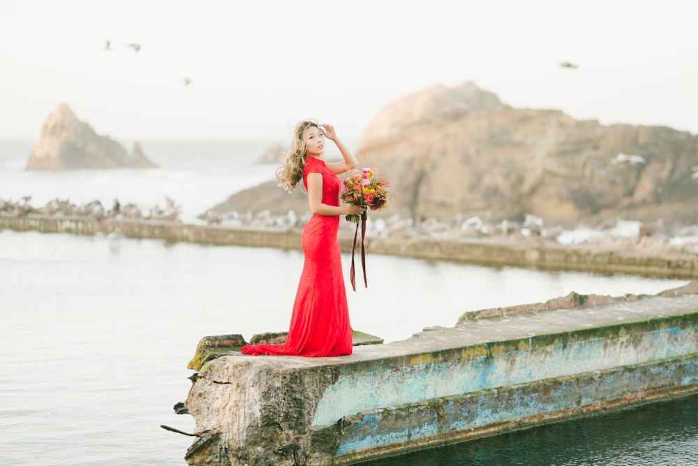woman in red dress standing on concrete dock during daytime