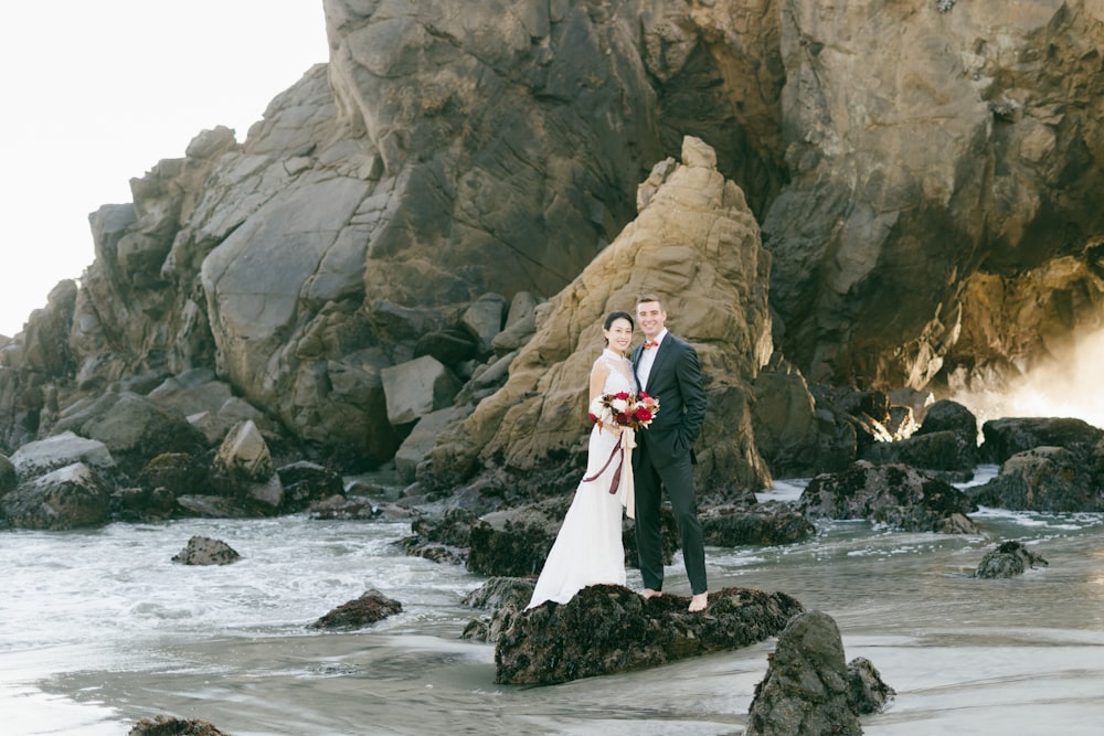 woman in white wedding gown standing on rock formation near body of water during daytime