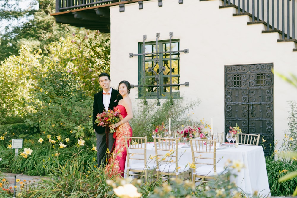 man in black suit and woman in red dress standing on green grass field