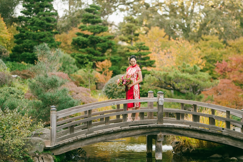 woman in red dress standing on wooden bridge over river during daytime