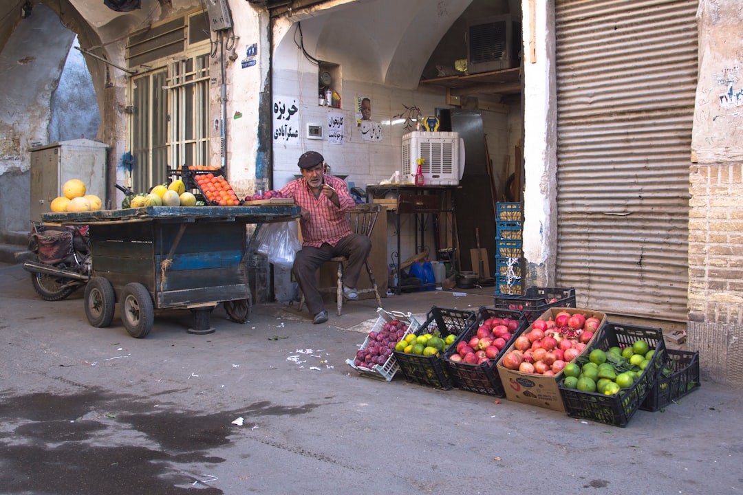 man in red and white stripe polo shirt standing beside fruit stand