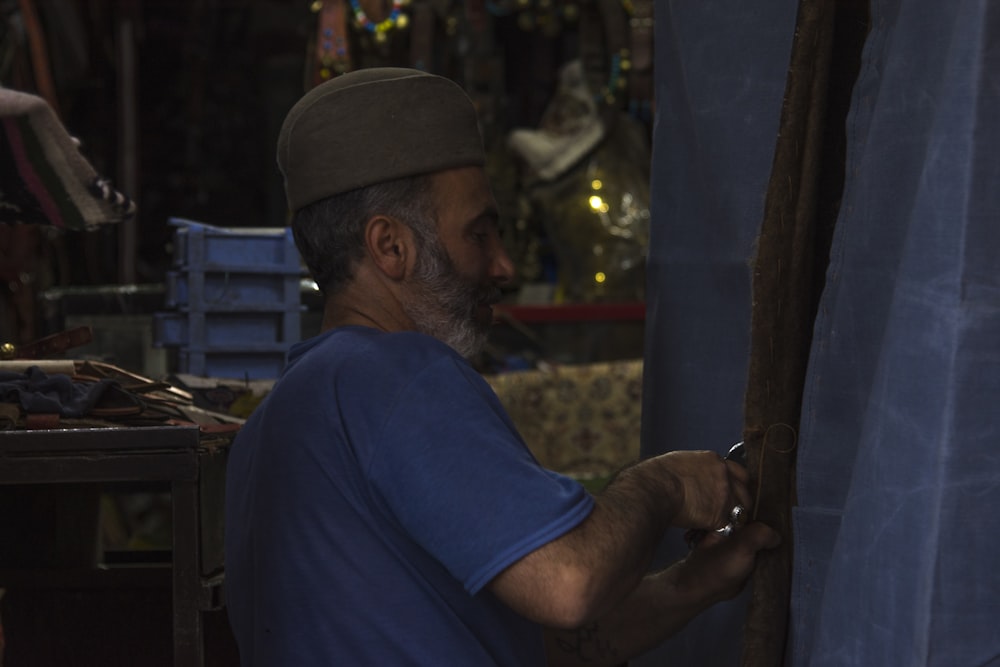 man in blue crew neck t-shirt and brown cap holding brown wooden stick