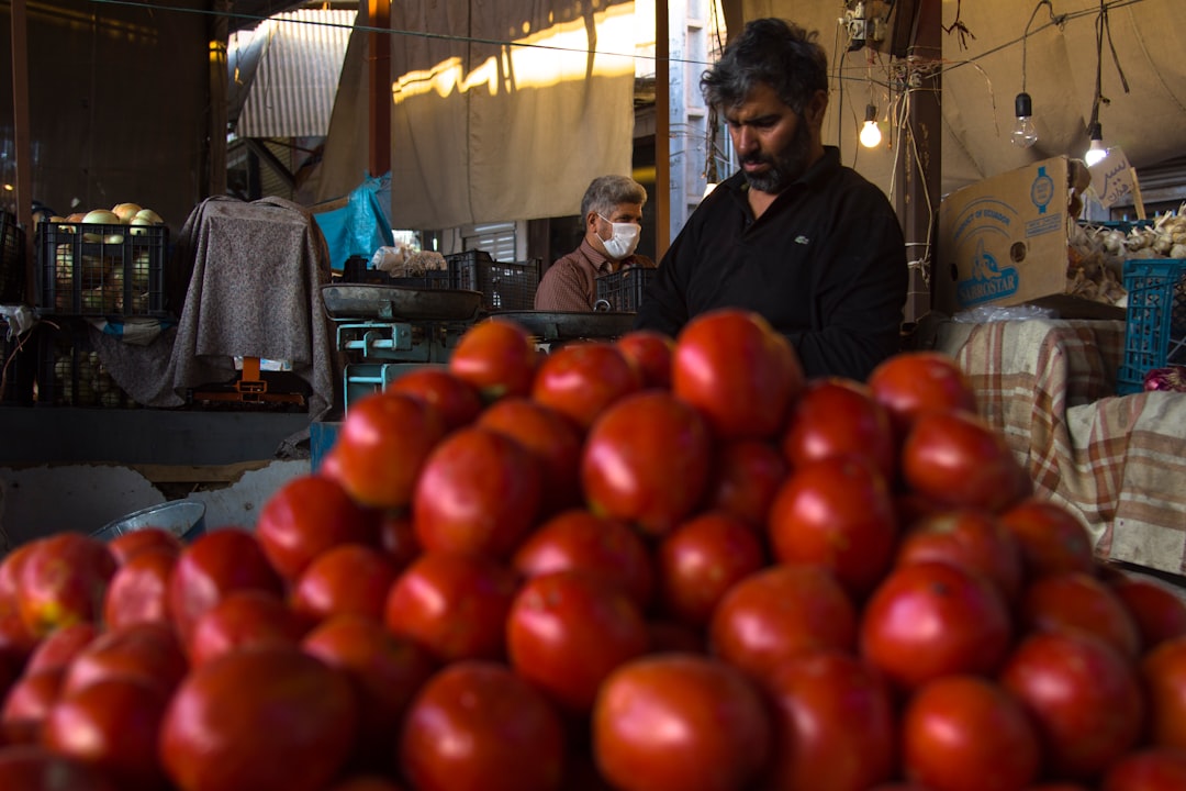 man in black jacket standing in front of red round fruits