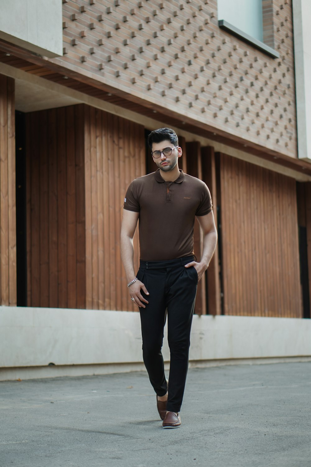 Hombre con camiseta sin mangas negra y pantalones negros con gafas de sol negras de pie sobre piso de concreto gris