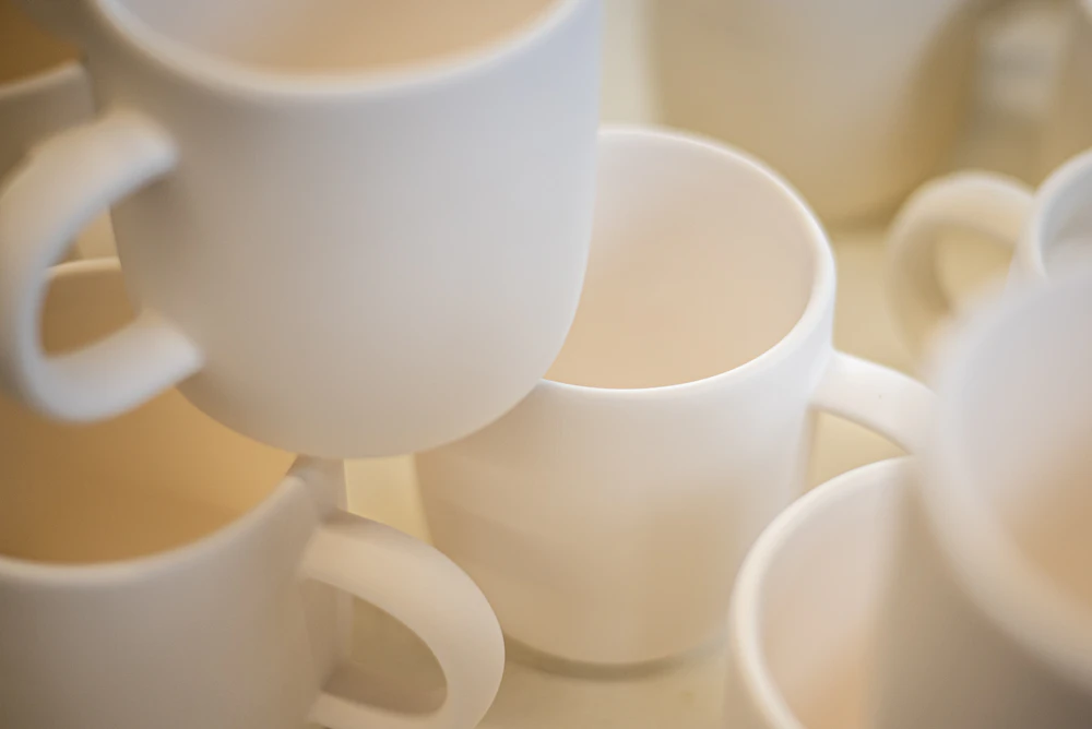Close-up of several white ceramic mugs clustered together, showing rims, handles, and interior curves