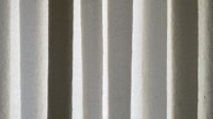 Vertical blinds with a crinkled texture appear as alternating light and dark bands. The material has a subtle sheen and displays a mix of soft white, gray, and beige colors.