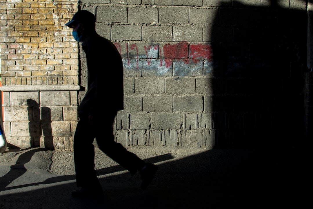 man in black hoodie walking on sidewalk during daytime